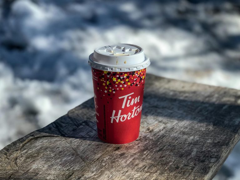 Red Tim Hortons paper cup sitting on a wooden table outdoors, surrounded by snow.