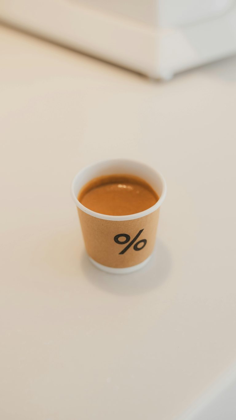 Simple close-up of espresso in a minimalist branded paper cup on a light background.